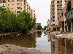 Vista de una calle despavimentada e inundada rodeada de edificios y escombros.